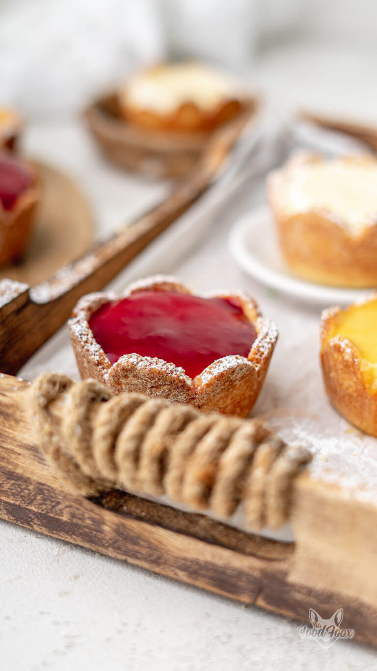 Nahaufnahme von Käsekuchen Muffins mit Quark und Erdbeerspiegel auf einem Holztablett.