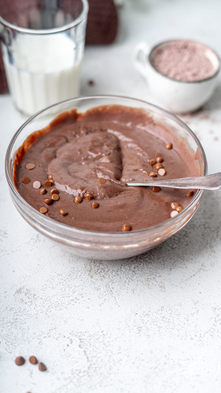 Nahaufnahme von selbstgemachtem Protein Pudding im Geschmack Schokolade. Der Pudding wurde mit kleinen Schokotropfen dekoriert und ein Löffel steckt drin.