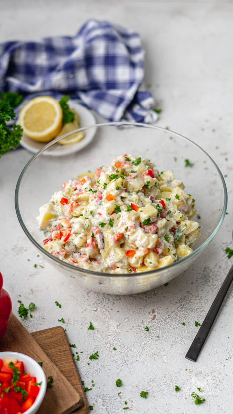 Selbstgemachter kalorienarmer Kartoffelsalat mit Joghurt und Gurke in einer Glasschüssel. Im Hintergrund ist eine angeschnittene Zitrone zu sehen.