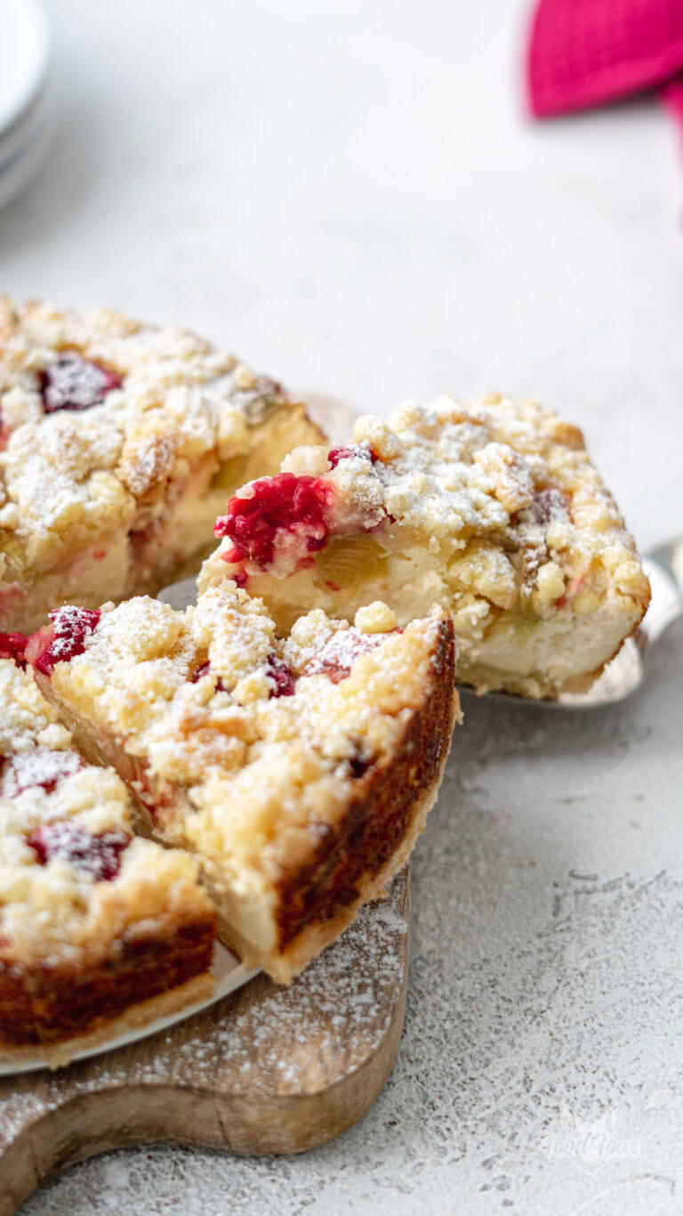 Nahaufnahme eines Stückchens Rhabarber Käsekuchen ohne Zucker mit Himbeeren.