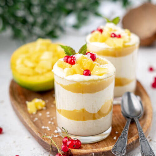 Ricpudding mit Mango-Mark und frischer Mango in einem Dessertglas. Garniert mit Kokosraspeln und roten Johannisbeeren.