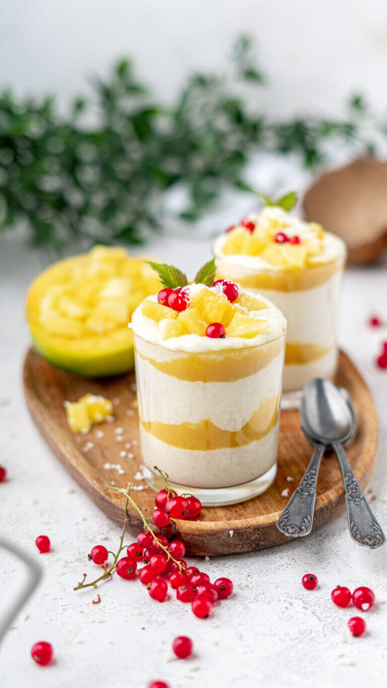 Ricpudding mit Mango-Mark und frischer Mango in einem Dessertglas. Garniert mit Kokosraspeln und roten Johannisbeeren.