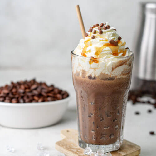 Eiskaffee ohne Zucker in einem hohen Glas. Getoppt mit frischer Sahne, Sirup und Schokolade.