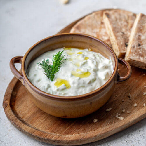 kalorienarmes griechisches Tsatsiki in einer braunen Servierschale garniert mit Dill und Olivenöl.