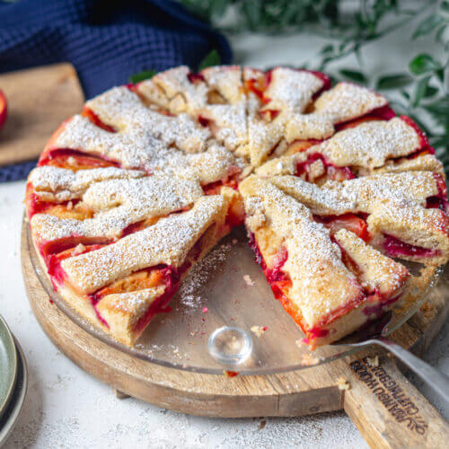 saftiger, kalorienarmer und zuckerfreie Pflaumenkuchen auf einem Glasteller, dieser steht auf einem Holzbrett. sieht sehr appetitlich aus.