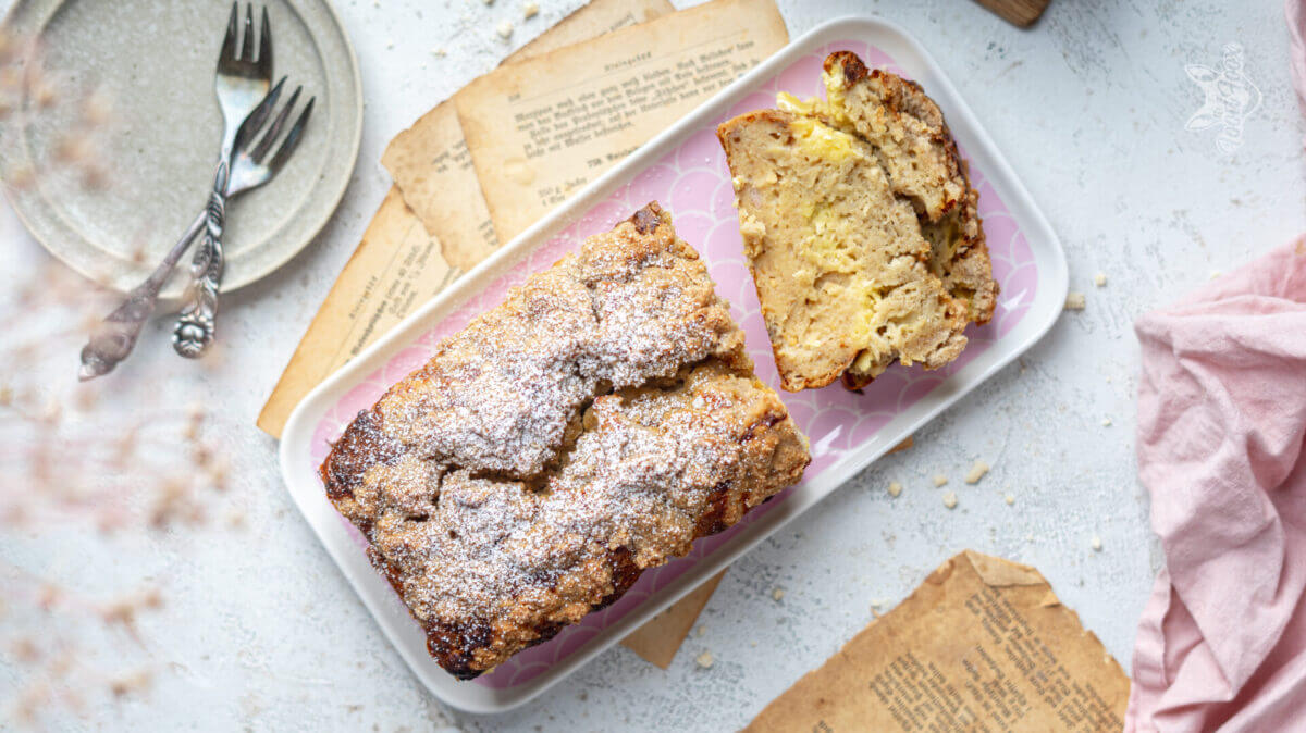 Draufsicht auf ein längliches highprotein Bananenbrot mit Streuseln. Zwei stücke wurden abgeschnitten und auf die Seite gelegt.