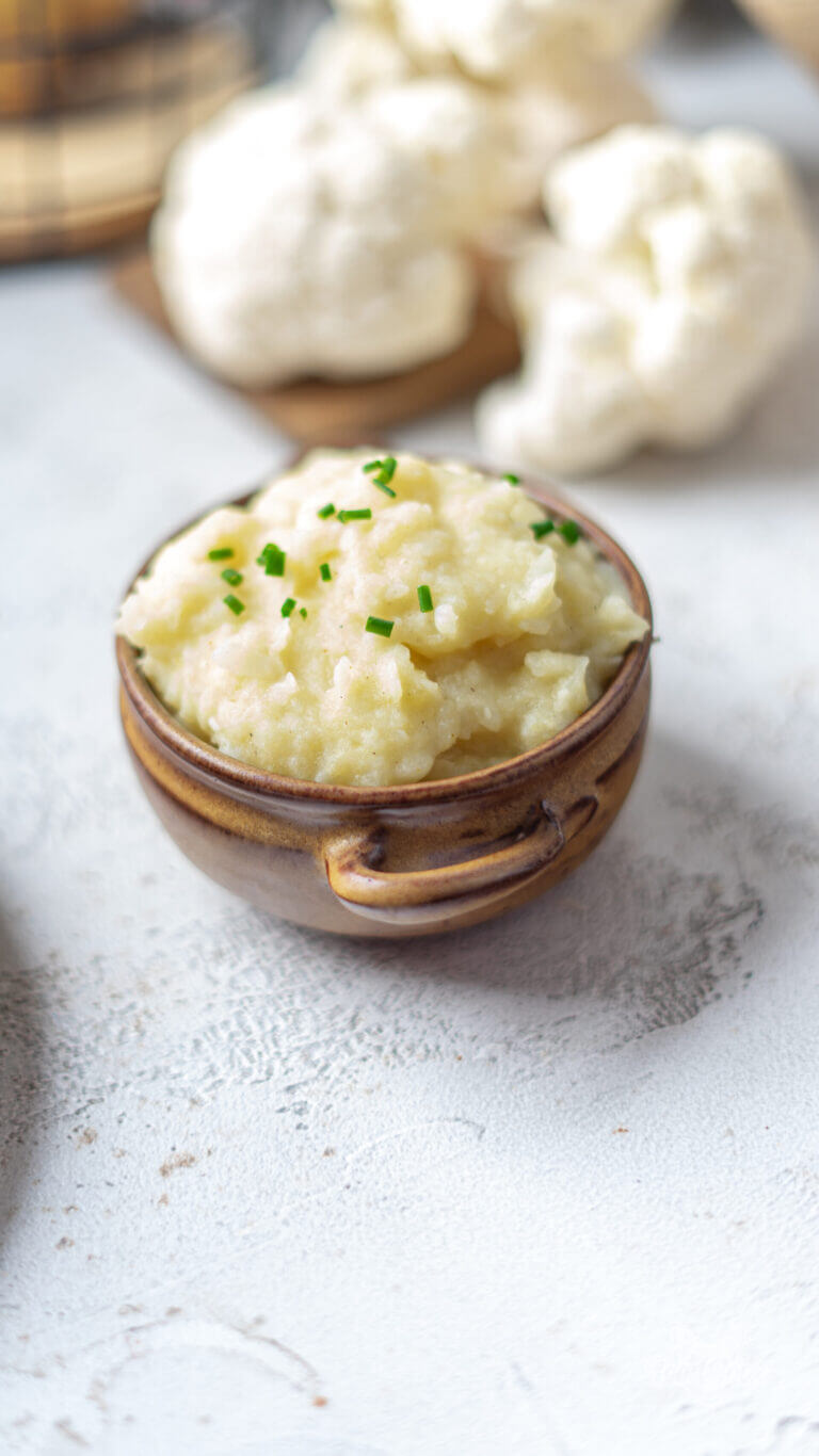 selbstgemachter, kalorienarmer Kartoffelbrei in einem kleinen Steinguttopf, verfeinert mit frischem Schnittlauch. Nahaufnahme.