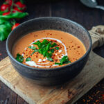 Kalorienarme Tomatensuppe zum Abnehmen in einer tiefen Schale, welche auf einem Holzbrettchen steht. Die Suppe wurde mit Basilikum, frischen Tomatenflocjen und Sahne verfeinert.