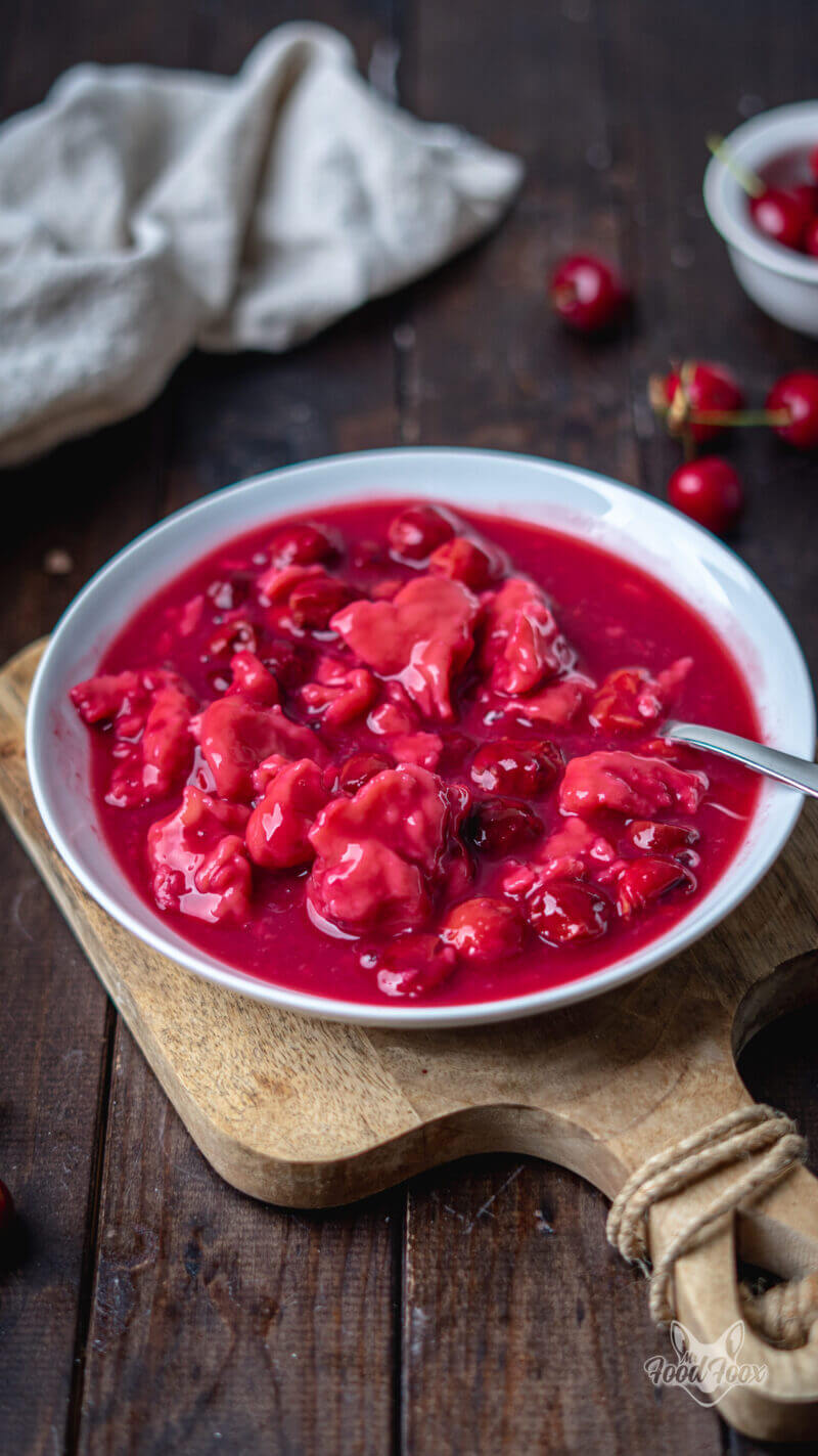 Kirschsuppe mit Klüten in einer weißen Schale auf einem Holzbrett: rote Kirschsuppe mit Mehlklößchen und frischen Kirschen, ein Leinentuch im Hintergrund sorgt für eine gemütliche Sommerstimmung.