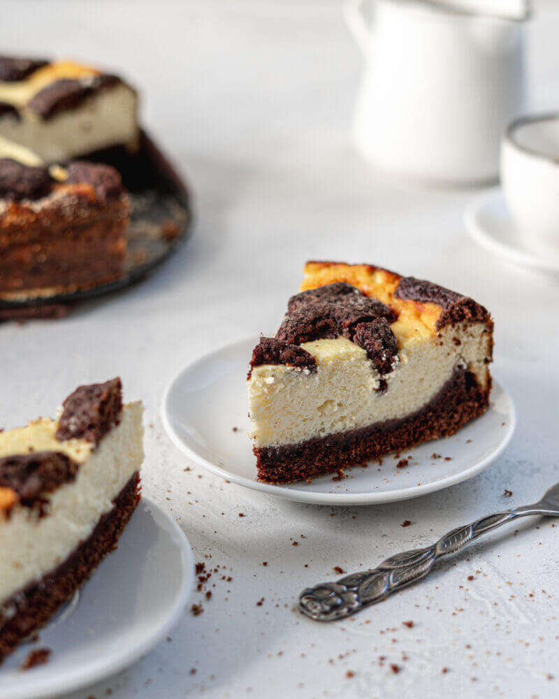 Ein Stück Russischer Zupfkuchen ohne Zucker auf einem weißen Teller, im Hintergrund der ganze Kuchen